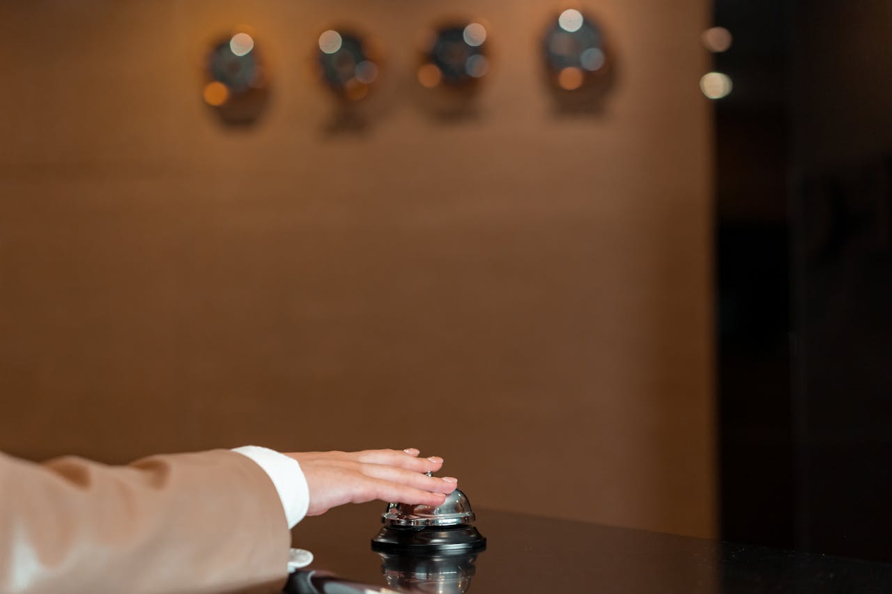 who-we-are A hand pressing a bell at a hotel reception, symbolizing service and hospitality.